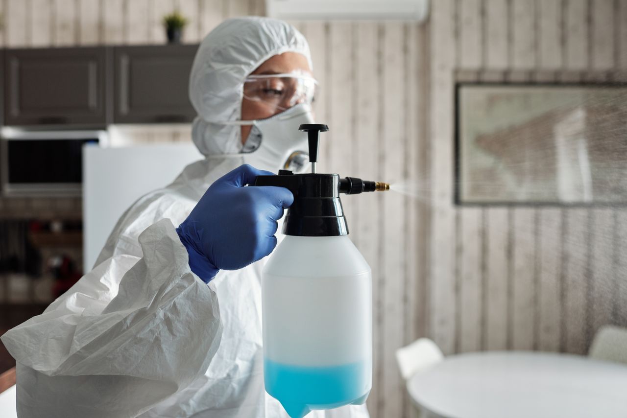 Professional in full gear disinfecting indoor area using a spray bottle for COVID-19 prevention.