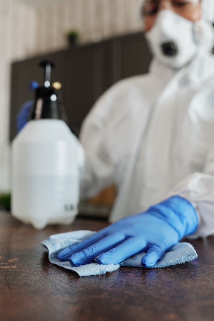 project-01-b Close-up of a professional in full protective gear disinfecting a surface indoors.