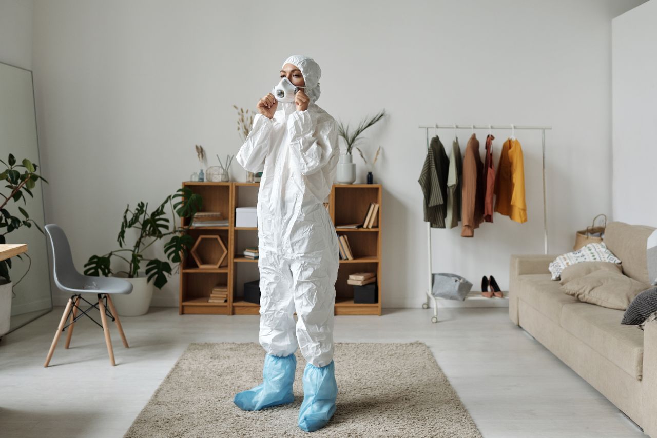 Woman in protective suit wearing face mask indoors with modern interior design.